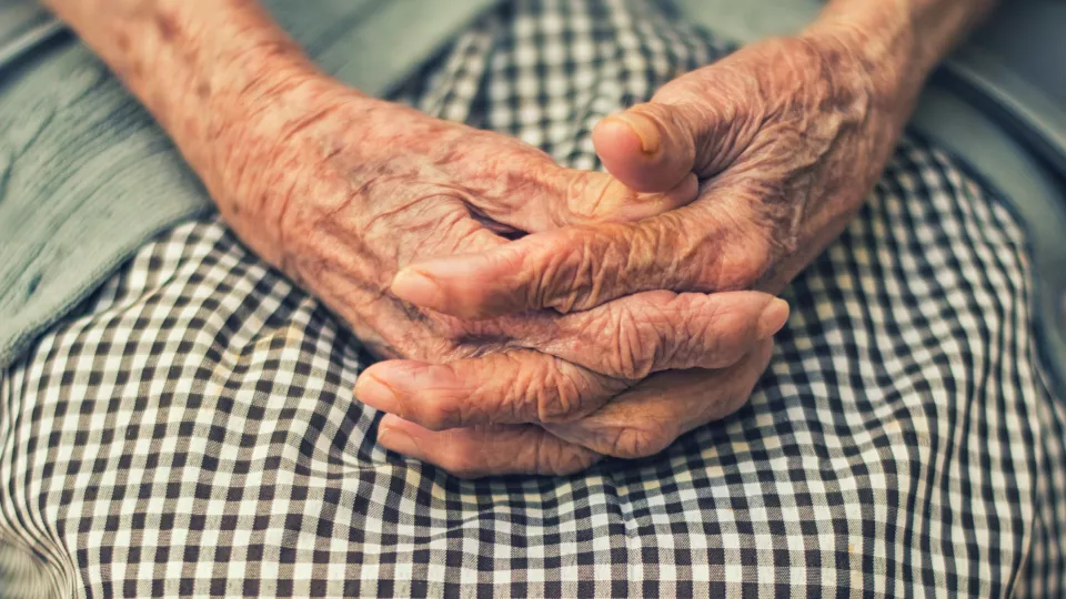 In zoomad bild på en äldre kvinna med händerna knäppta placerade i knät. Foto. 
