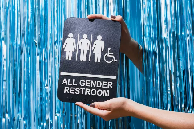 En person håller upp en toalettskylt med symboler för olika könstillhörigheter. Foto. 